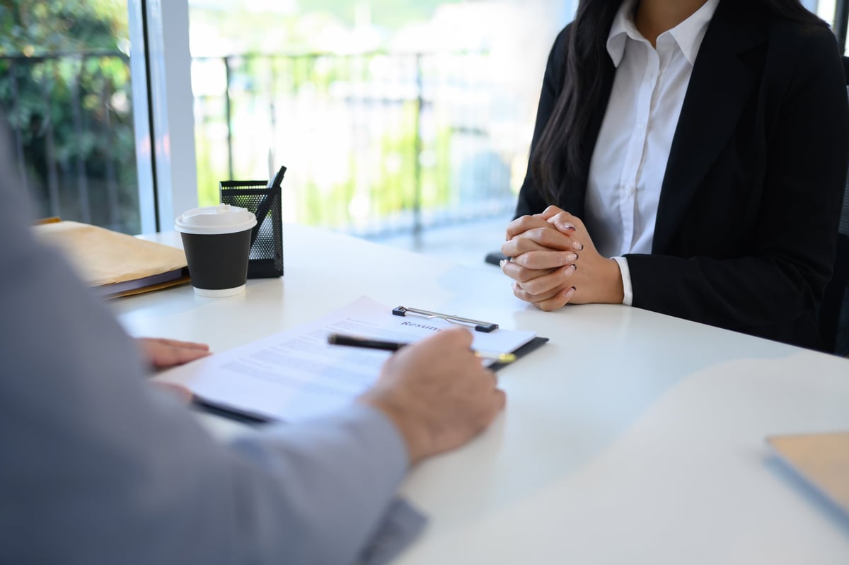 Candidate in formal wear attentively sitting across from an interviewer reviewing her resume.