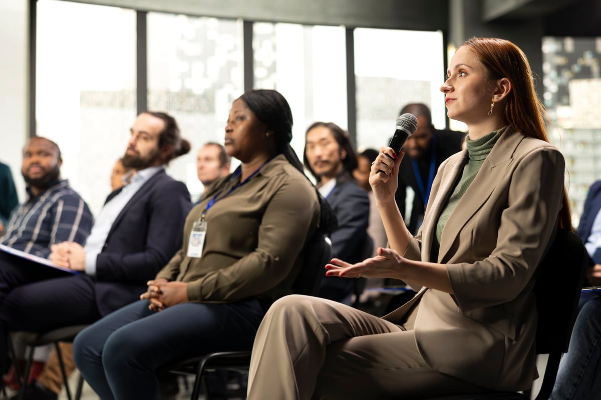 Young adult businesswoman in audience interacting with presenter, asking questions and engaging in debate