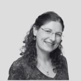 Black and white portrait of a smiling woman with curly dark hair and glasses wearing a textured dark shirt