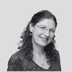 Black and white portrait of a smiling woman with curly dark hair and glasses wearing a textured dark shirt